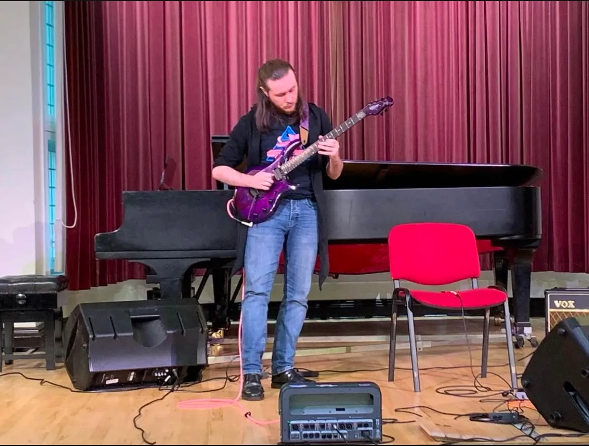 Jamie performing on electric guitar beside a grand piano